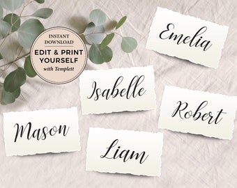May include: Five white place cards with torn edges, each with a name written in black cursive script: Mason, Isabelle, Liam, Robert, Emelia. The cards are on a white textured surface with green eucalyptus leaves in the background.