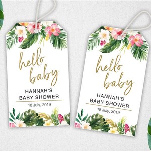 Puede incluir: Dos etiquetas de regalo blancas con dise&ntilde;os florales tropicales y letras doradas. El texto en las etiquetas dice "hello baby" y "Hannah's Baby Shower" con la fecha "18 de julio de 2019".