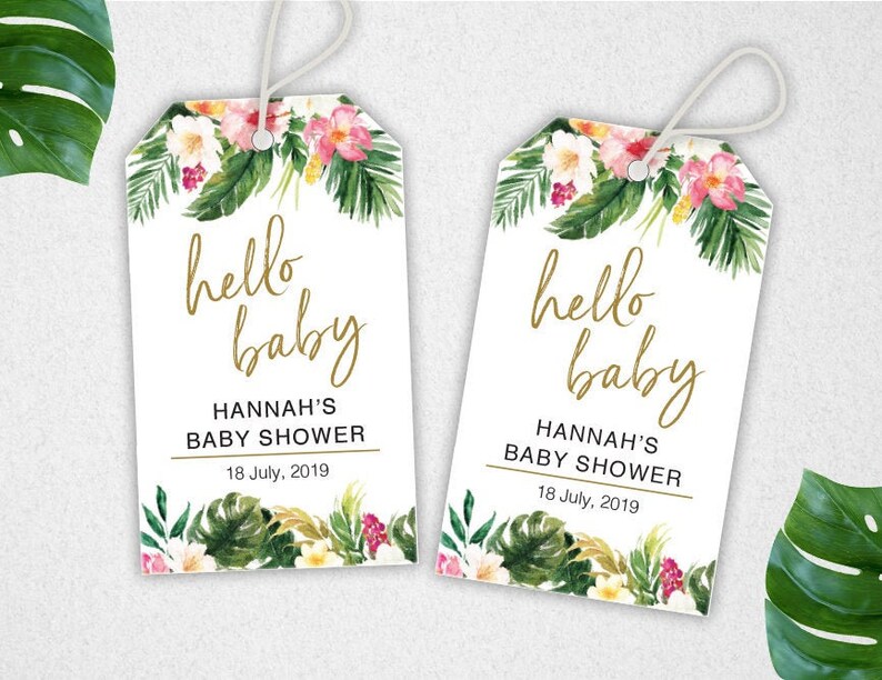 Puede incluir: Dos etiquetas de regalo blancas con dise&ntilde;os florales tropicales y letras doradas. El texto en las etiquetas dice "hello baby" y "Hannah's Baby Shower" con la fecha "18 de julio de 2019".