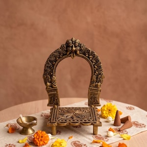 Peut inclure: Un support en métal de couleur laiton en forme de trône, doté d'un dossier arqué aux sculptures complexes et d'une base carrée à motif floral. Le support est entouré de fleurs de souci jaunes et orange éparpillées et de trois cônes d'encens.