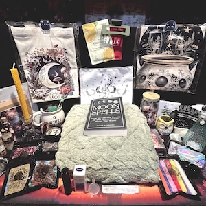 Peut inclure: Un ensemble d'objets comprenant un livre Moon Spells, une couverture vert sauge texturée, un sac fourre-tout blanc avec un motif de lune et de fleurs, un sac noir avec une illustration de chaudron, une bougie en cire d'abeille jaune et des accessoires.