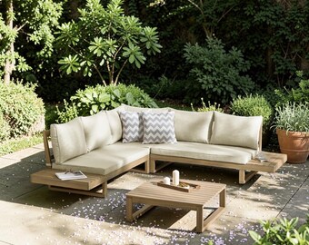 May include: An L-shaped outdoor sectional sofa made of light brown wood with beige cushions and two gray and white chevron patterned throw pillows, accompanied by a matching square wooden coffee table with a small tray holding two white candles.
