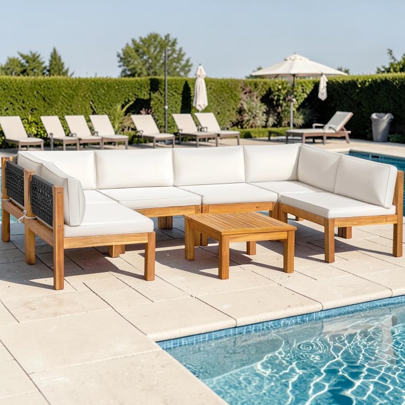 May include: A modular outdoor sectional sofa set with a light brown wooden frame, white cushions, and black woven side panels. The set includes a corner sofa configuration and a matching square wooden coffee table positioned on a patio by a pool.