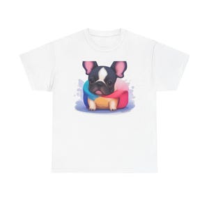 Może przedstawiać: Biały t-shirt z wyśrodkowaną grafiką przedstawiającą czarno-białego szczeniaka buldoga francuskiego. Szczeniak jest owinięty w kolorowy, wielobarwny kocyk w odcieniach niebieskiego, żółtego i różowego, na jasnym i delikatnym tle.