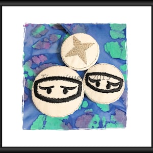 May include: Three white fabric circles with embroidered designs. One circle has a silver star, another has a black eye design, and the third has a black eye design with a small black dot in the center.
