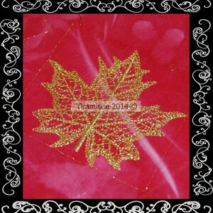 May include: A gold glitter maple leaf design on a red fabric background. The leaf is detailed and intricate, with a delicate lace-like pattern. The text "Tiramisu 2014" is visible in the center of the leaf.