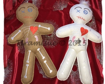 May include: Two voodoo dolls, one brown and one white, with red hearts and stitched-on details. The dolls are lying on a red velvet background with silver glitter.
