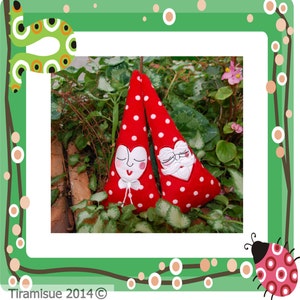 May include: Two red felt ornaments with white polka dots and embroidered faces. One ornament has a heart-shaped face with a smiling mouth and closed eyes. The other ornament has a beard and a mustache.