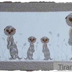 May include: A white and gray quilted wall hanging featuring five embroidered meerkats standing on their hind legs. The meerkats are arranged in a line, with the largest meerkat on the right and the smallest meerkat on the left. The meerkats are all facing forward, with their tails curled behind them. The background is a light blue color, and the meerkats are surrounded by white embroidered grass.