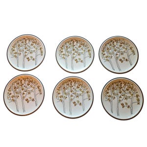 May include: A set of six round ceramic plates, each featuring a white background with a black-lined illustration of a tree with brown and tan leaves. Each plate has a thin dark rim, creating a uniform appearance across the entire collection.