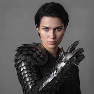 May include: A dark metallic shoulder pauldron and matching gauntlet featuring an overlapping scale-like design. The armour pieces are constructed from individual dark grey metal plates secured with rivets, covering the shoulder and the entire forearm.