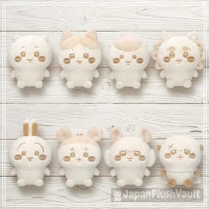 May include: A collection of eight small, off-white plush toys arranged in two rows. Each soft figure features embroidered facial details, including large eyes, a small mouth, and rosy cheeks, with distinct head shapes representing various animal characters.