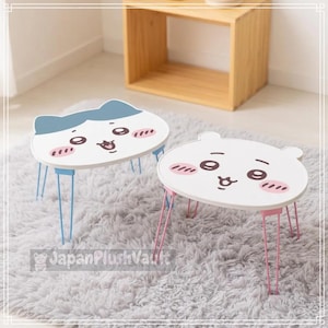 May include: Two small, low-profile tables with white, cat-shaped tabletops featuring cartoon faces with pink cheeks. One table has blue metal legs and a blue cat-ear top, while the other has pink metal legs and a white cat-ear top.