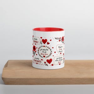 May include: A white ceramic mug with a bright red interior featuring a repeating pattern of red hearts, floral accents, and French text including phrases like je suis CAPABLE, je suis là où je dois être, Respire Crois Avance, and je suis CONFIANTE.