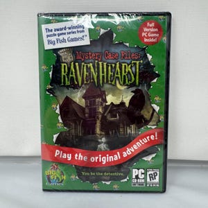 May include: A PC game case for Mystery Case Files: Ravenhearst. The green cover features a dark mansion, a raven, and a ghost-like figure. Text includes 'The award-winning puzzle game series from Big Fish Games!', 'Full Version PC Game Inside!', and 'Play the original adventure!'