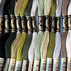 May include: A selection of embroidery threads in a range of colours, from white and grey to black and various greens and tans. Each spool is labelled with a black and gold band and a barcode. The threads are neatly wound.