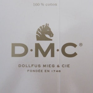 May include: A white label with a gold logo for DMC, a company that makes embroidery floss. The logo features a stylized horse's head and the text "D.M.C.  DOLLFUS MIEG & CIE FOND&Eacute;E EN 1746". The label also has the text "100% coton" and "ART. 117" in blue.