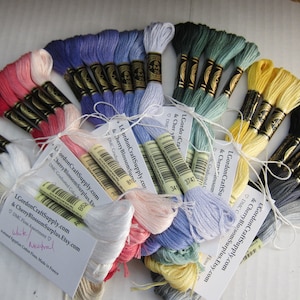 May include: A collection of embroidery floss spools in various colours, including red, pink, white, blue, green, yellow, grey, and black. The spools are tied together with string and labelled with the company name "LGordonCraftSupply.com & Cherry Blossom Surplus.Etsy.com".