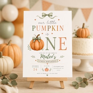 May include: A white rectangular birthday invitation sign featuring a watercolour pumpkin, a sage green bow, and the text "our little PUMPKIN is ONE" with "Mateo's FIRST BIRTHDAY" and event details including date, time, and location on a wooden easel.