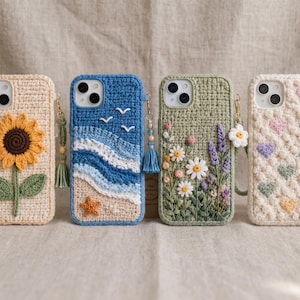 May include: Four smartphone cases with crochet covers. The first is beige with a yellow sunflower. The second is blue with a beach, ocean waves, and a starfish. The third is sage green with embroidered wildflowers. The fourth is cream with pastel hearts.