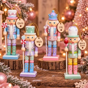 May include: Four wooden nutcracker ornaments in pastel colours, each featuring a unique hat, a staff with a candy-themed topper, and a small round wooden tag. The tags are personalised with the names Olivia, Myla, Lily, and the phrase Merry Xmas.