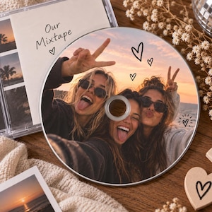 Op de afbeelding: Een ronde, op maat bedrukte cd met een foto van drie personen die bij zonsondergang het vredesteken maken en hun tong uitsteken. De cd bevat handgetekende hartjes. Een cd-hoesje bevat de tekst Our Mixtape en een hartje.