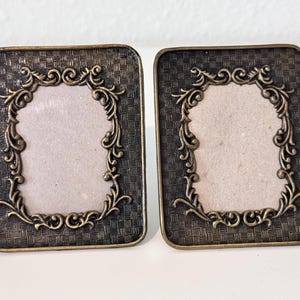 May include: Two rectangular picture frames with a dark bronze finish and a textured, woven-style background. Each frame features an ornate, raised scrollwork border surrounding a central rectangular opening with a light beige insert.