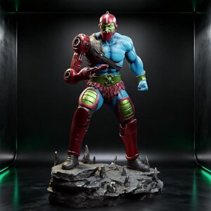 May include: A muscular action figure with blue skin and a green face, wearing a red helmet and armor. The figure features a mechanical red right arm, a green belt with a skull emblem, and red leg armor, standing on a jagged gray rock base.