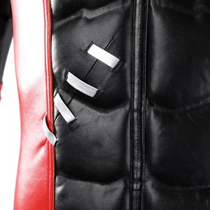 Pu&ograve; includere: Un indumento in similpelle rossa e nera caratterizzato da una sezione del busto imbottita con una cucitura centrale verticale. Il lato destro del petto presenta tre cinghie bianche orizzontali integrate nel pannello nero, creando un effetto.