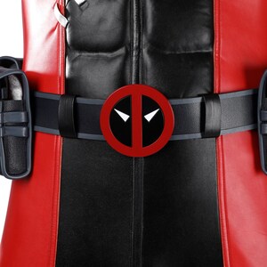 Pu&ograve; includere: Una cintura multiuso nera e rossa con una fibbia circolare rossa, un centro nero e forme bianche simili a occhi. La cintura include due tasche nere sui lati ed &egrave; indossata sopra una tuta rossa e nera dall'aspetto testurizzato e imbottito.