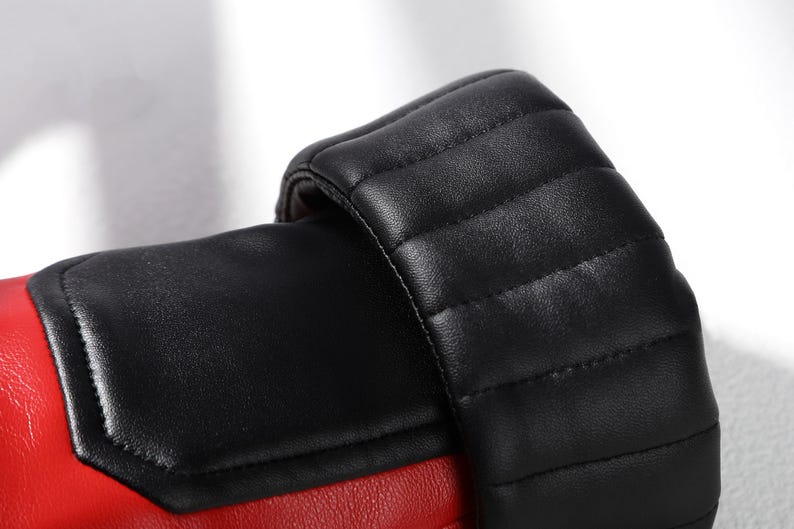 Pu&ograve; includere: Un guantone da boxe con un corpo principale rosso vivace e un polsino nero a contrasto. Il polsino presenta cuciture trapuntate orizzontali, mentre la sezione principale ha un pannello nero liscio integrato sulla superficie rossa.