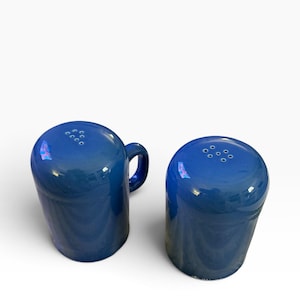 May include: A pair of glossy cobalt blue ceramic shakers. One shaker features a small side handle and the letter F embossed on the top, while the other shaker has a smooth top. Both items have a series of small holes for dispensing contents.
