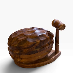 May include: A dark brown wooden nutcracker shaped like a large walnut, featuring a textured, carved surface. The set includes a matching wooden mallet that stands upright on a small, integrated wooden base attached to the side of the nutcracker.
