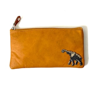 May include: A rectangular mustard yellow leather pouch featuring a top zipper closure with a brown leather pull tab. An embroidered patch of a dark gray elephant with white tusks and accents is positioned on the lower right side of the pouch.
