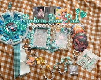 May include: A Custom Bias Pack featuring a teal ribbon rosette, two decorated photo frames with pearls and beads, four circular character badges, two beaded keychains with heart-shaped clasps, and a small character sticker in a plastic sleeve.