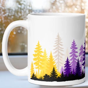 May include: A white ceramic mug featuring a printed forest landscape design. The graphic displays a row of pine trees in varying shades of yellow, light gray, purple, and dark violet, with a solid black silhouette of ground foliage at the base.