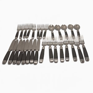 May include: A large flatware set consisting of stainless steel knives, forks, and spoons. Each piece features a polished silver-tone metal head and a solid black handle with a subtle horizontal grooved detail at the base of the handle.