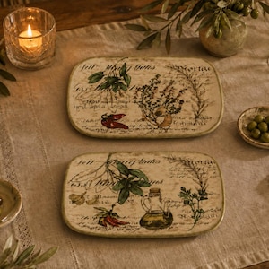 May include: Two rectangular ceramic serving platters featuring a cream-colored base with vintage-style botanical illustrations of herbs, chili peppers, garlic, and an oil cruet, accented by cursive script text overlays in a dark brown ink.