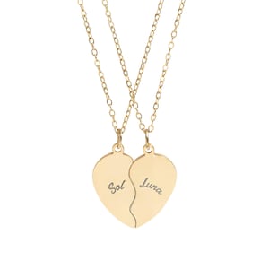 Peut inclure: Un ensemble de colliers dorés composé de deux pendentifs en forme de cœur qui s'assemblent. Chaque pendentif est suspendu à une fine chaîne dorée. Le pendentif gauche porte l'inscription Sol et le droit porte l'inscription Luna.
