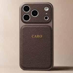 Puede incluir: Una funda de teléfono de cuero marrón oscuro con acabado texturizado y marco metálico. La parte posterior presenta el nombre CARO grabado en letras doradas. El área del módulo de cámara también está cubierta de cuero texturizado.