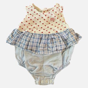 Può includere: Una tutina senza maniche con corpetto bianco a fantasia di cuori rossi e una piccola toppa con logo GUESS. La vita è accentuata da un peplum a balze a quadri blu e bianchi, mentre la parte inferiore è realizzata in tessuto seersucker blu e bianco.