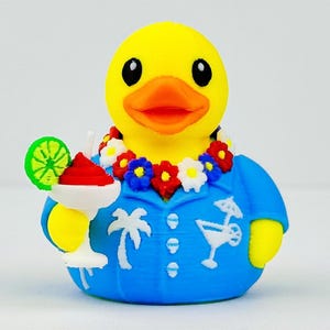 May include: A yellow rubber duck wearing a blue shirt with white palm tree and cocktail graphics, a floral lei with red, white, and blue flowers, and holding a white cocktail glass with a red drink and a green lime slice garnish.