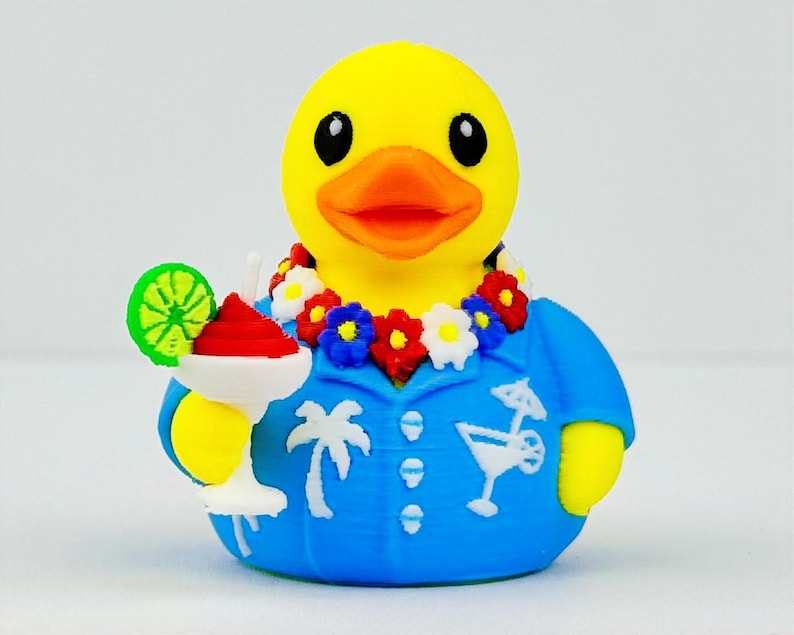 May include: A yellow rubber duck wearing a blue shirt with white palm tree and cocktail graphics, a floral lei with red, white, and blue flowers, and holding a white cocktail glass with a red drink and a green lime slice garnish.
