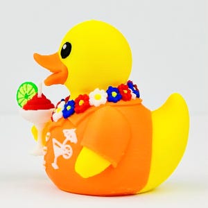 May include: A yellow rubber duck wearing an orange shirt with a white cocktail graphic, a floral lei with red, white, and blue flowers, and holding a white cocktail glass topped with a green lime slice. The duck has an orange beak and black eyes.