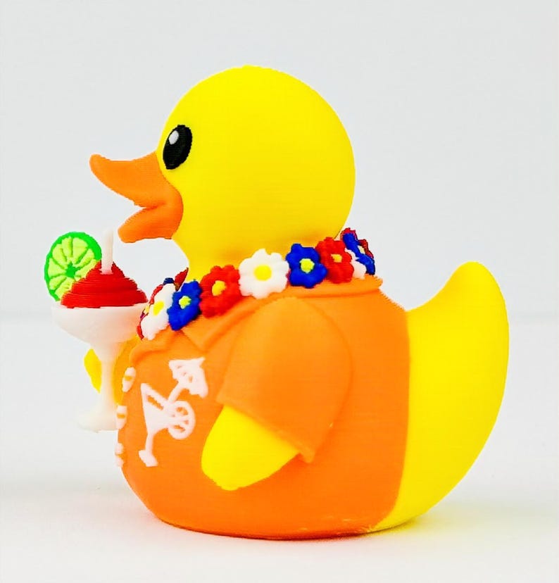 May include: A yellow rubber duck wearing an orange shirt with a white cocktail graphic, a floral lei with red, white, and blue flowers, and holding a white cocktail glass topped with a green lime slice. The duck has an orange beak and black eyes.
