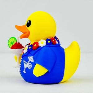 May include: A yellow rubber duck wearing a blue shirt with a white cocktail graphic print. The duck has a colorful floral lei around its neck and is holding a white cocktail glass with a red drink and a green lime slice garnish.