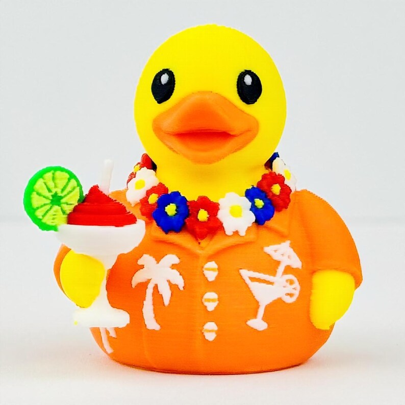 May include: A yellow rubber duck wearing an orange shirt with white palm tree and cocktail graphics. The duck has an orange beak, black eyes, and a colorful floral lei around its neck. It holds a white cocktail glass with a lime slice garnish.