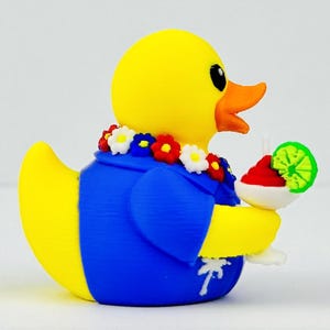 May include: A yellow rubber duck wearing a blue shirt with a white palm tree print and a colorful floral lei around its neck. The duck holds a white cocktail glass containing a red drink garnished with a bright green lime slice in its wing.