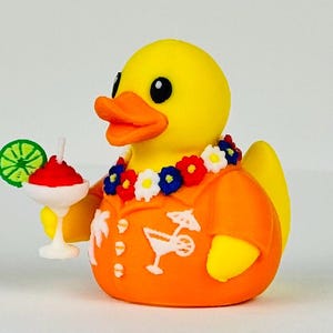 May include: A yellow rubber duck wearing an orange short-sleeved shirt with white palm tree and cocktail graphics. The duck has a floral lei around its neck and holds a white cocktail glass with a red drink, a white straw, and a green lime slice.