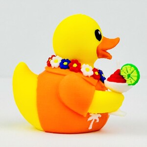 May include: A yellow rubber duck wearing an orange shirt with a white palm tree print and a colorful floral lei around its neck. The duck holds a white cocktail glass containing a red drink garnished with a bright green lime slice.